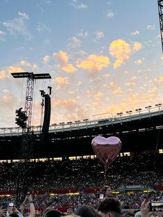 a large crowd at a concert with one person holding up a heart shaped balloon