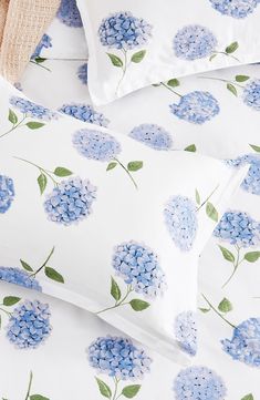 a bed with blue flowers and green leaves on the pillowcase, along with two pillows