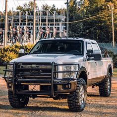 a silver truck parked on top of a dirt field next to power lines and trees