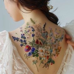 the back of a woman's neck with flowers painted on her body and behind her is a white lace dress