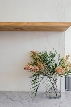 two vases with flowers on a marble counter top next to a shelf above them