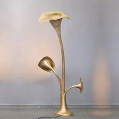 a gold colored floor lamp with two large flowers on it's base and one flower shaped like an antelope