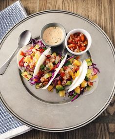 a plate topped with tacos and sauces on top of a wooden table next to a fork