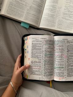 an open bible on top of a bed next to a person's hand holding it