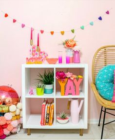 a white shelf filled with lots of colorful items next to a chair and potted plant