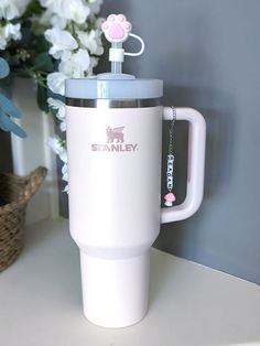 a white coffee cup with a pink dog on the lid and handle sitting next to flowers