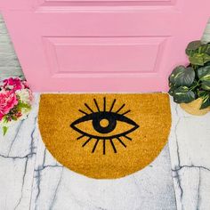 a door mat with an eye drawn on it next to a potted plant and pink door