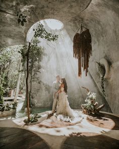 a man and woman are sitting on the floor in front of a waterfall with plants