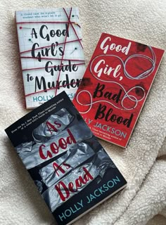 two books sitting on top of a bed next to each other, one is red and the other is black