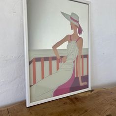 a woman wearing a hat sitting on a bench in front of a white wall and wooden table