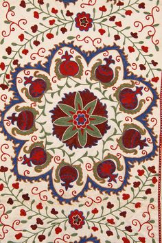 an intricately designed rug with red and green flowers on white ground, in the middle of