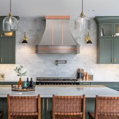 a kitchen with green cabinets and marble counter tops, copper hoods over the range