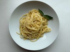 a white plate topped with pasta and sauce on top of a wooden table next to a green leaf