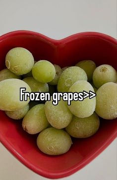 a red bowl filled with green grapes in the shape of a heart on top of a white table