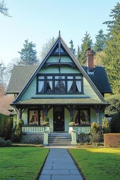 a green house with black trim on the roof and windows, along with a walkway leading to the front door