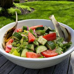 a white bowl filled with cucumbers and other vegetables on top of a wooden table