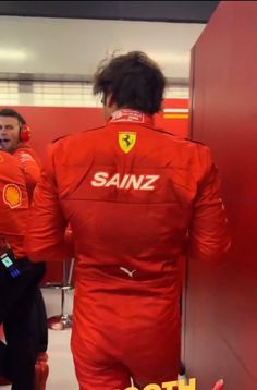 two men in red racing suits talking to each other