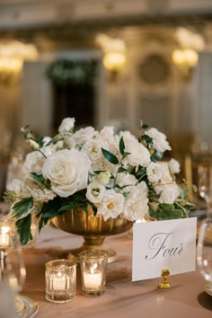 a centerpiece with white flowers and greenery on a table