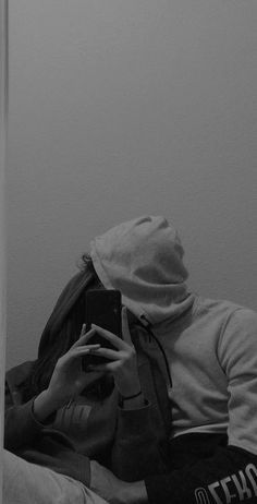 black and white photograph of a person sitting on a bed looking at their cell phone