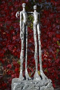 a statue of two people standing next to each other in front of a red bush