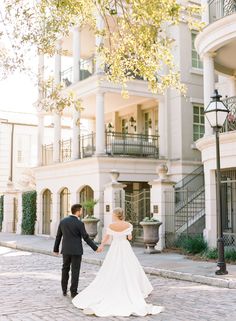 a bride and groom holding hands walking down the street in front of an elegant building