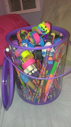 a purple plastic container filled with lots of pens and pencils on top of a bed