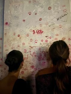 two girls are writing on a wall with lipstick