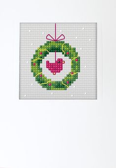 a cross stitch christmas ornament hanging on a white wall with a pink ribbon