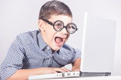 a young boy wearing glasses and using a laptop with his mouth wide open to look at the screen