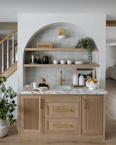 an open kitchen with wooden cabinets and marble counter tops, along with shelves that have plants on them