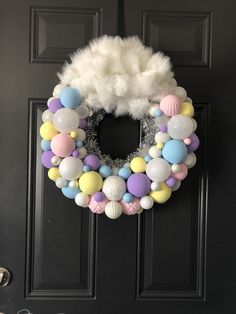 a wreath made out of balloons and white feathers on a black door with the words happy birthday written in it