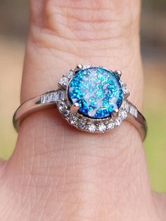 a close up of a person's hand holding a ring with a blue and white stone