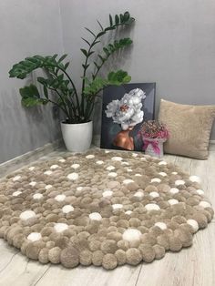 a round rug with white balls on the floor next to a potted plant and two pictures