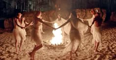 four women dancing around a campfire in the sand at night with their arms wrapped around each other