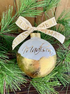 a personalized christmas ornament hanging from a pine tree with a ribbon on it