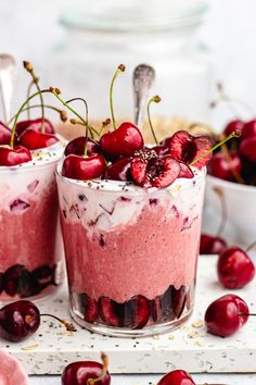 two desserts with cherries and whipped cream in them on a white surface surrounded by cherries