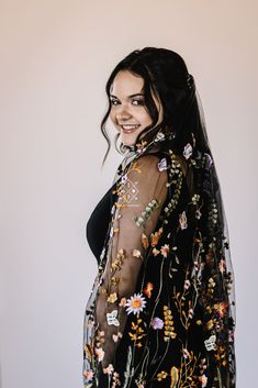 a woman wearing a black dress with flowers on it and a veil over her head