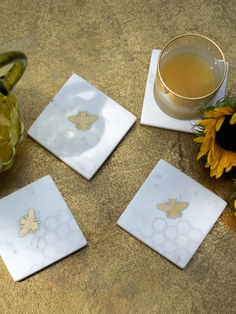 three coasters with bees on them next to a cup of tea and sunflowers