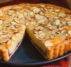 a pie with almonds on top is sitting on a black plate and has one slice missing from it