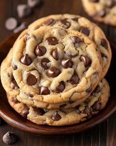 three chocolate chip cookies stacked on top of each other in a wooden bowl with chocolate chips scattered around them