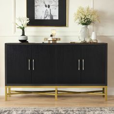 a black and gold sideboard with two vases on top of it next to a framed photograph