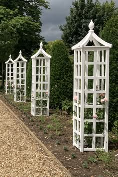 four white garden arbors lined up on the side of a road with roses growing in them