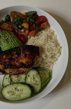 a white plate topped with meat, rice and veggies next to cucumbers