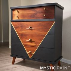 a black and brown chest of drawers with gold accents on the top, in front of a white wall