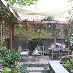 an outdoor dining area with tables and chairs surrounded by greenery, shrubs and flowers