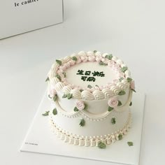 a white cake decorated with pink flowers and green leaves on top of a card board