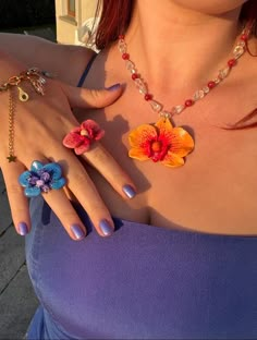 a woman with red hair wearing two rings and necklaces on her chest, one ring has an orange flower in the middle