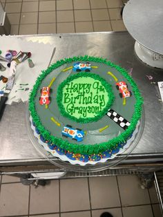 a birthday cake with green frosting and race cars on the top is ready to be cut