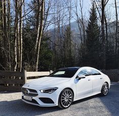 a white mercedes benz cla parked in front of some trees and fenced area