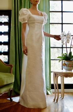 a woman standing in front of a window wearing a white dress with puffed sleeves